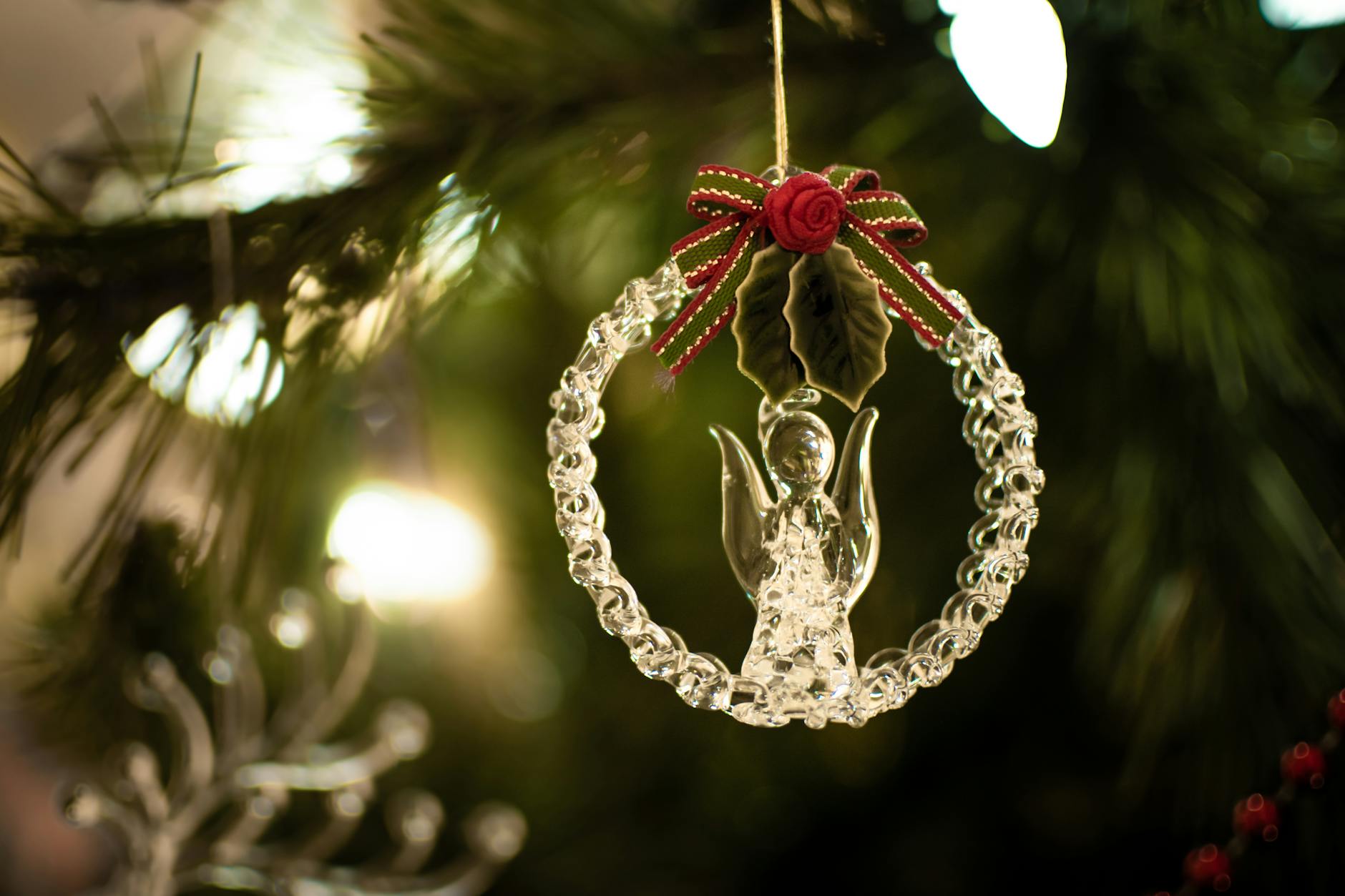 A delicate glass angel ornament with a red ribbon adorns a festive Christmas tree.