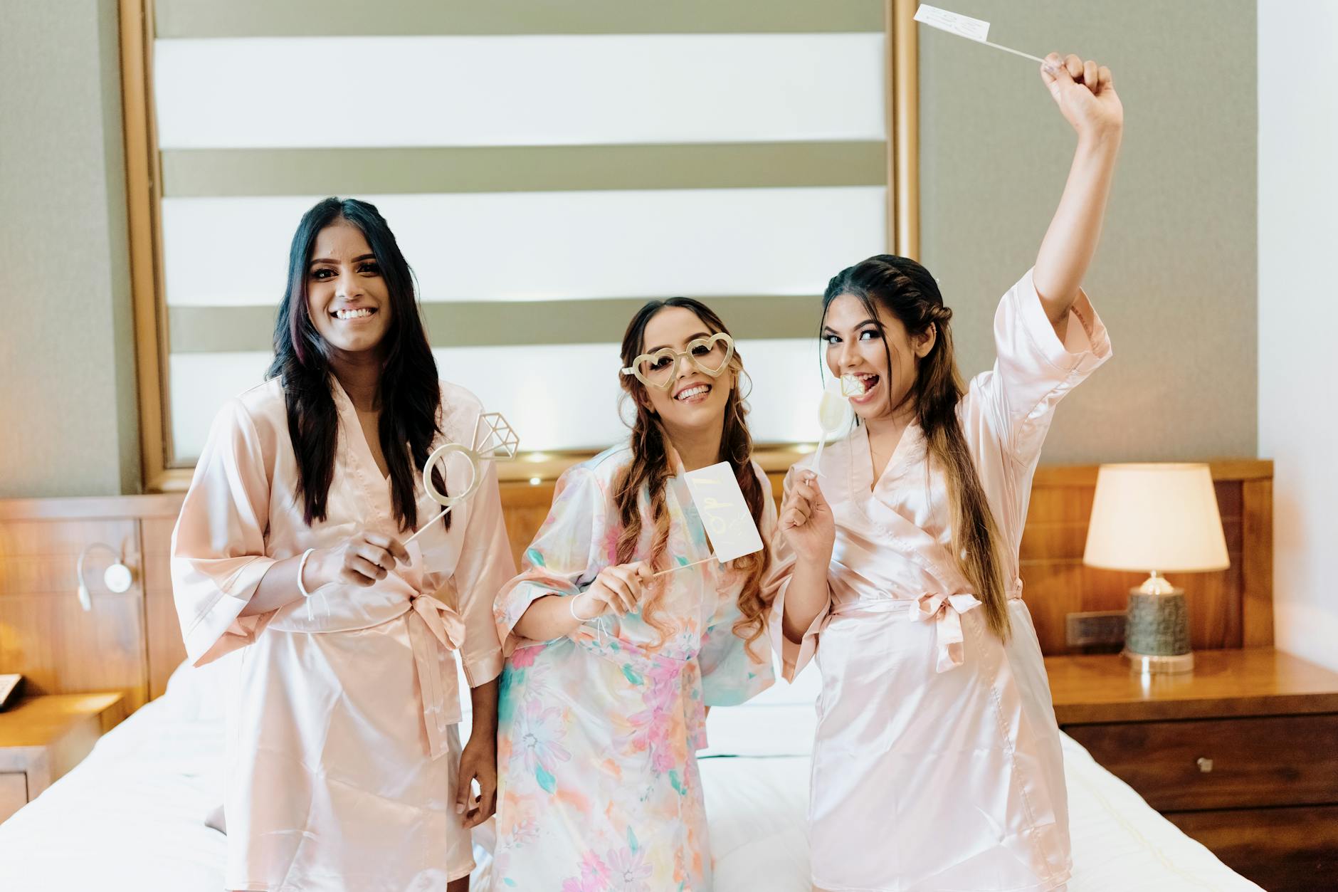 Three women in bathrobes enjoying a bridal shower indoors, celebrating with props.
