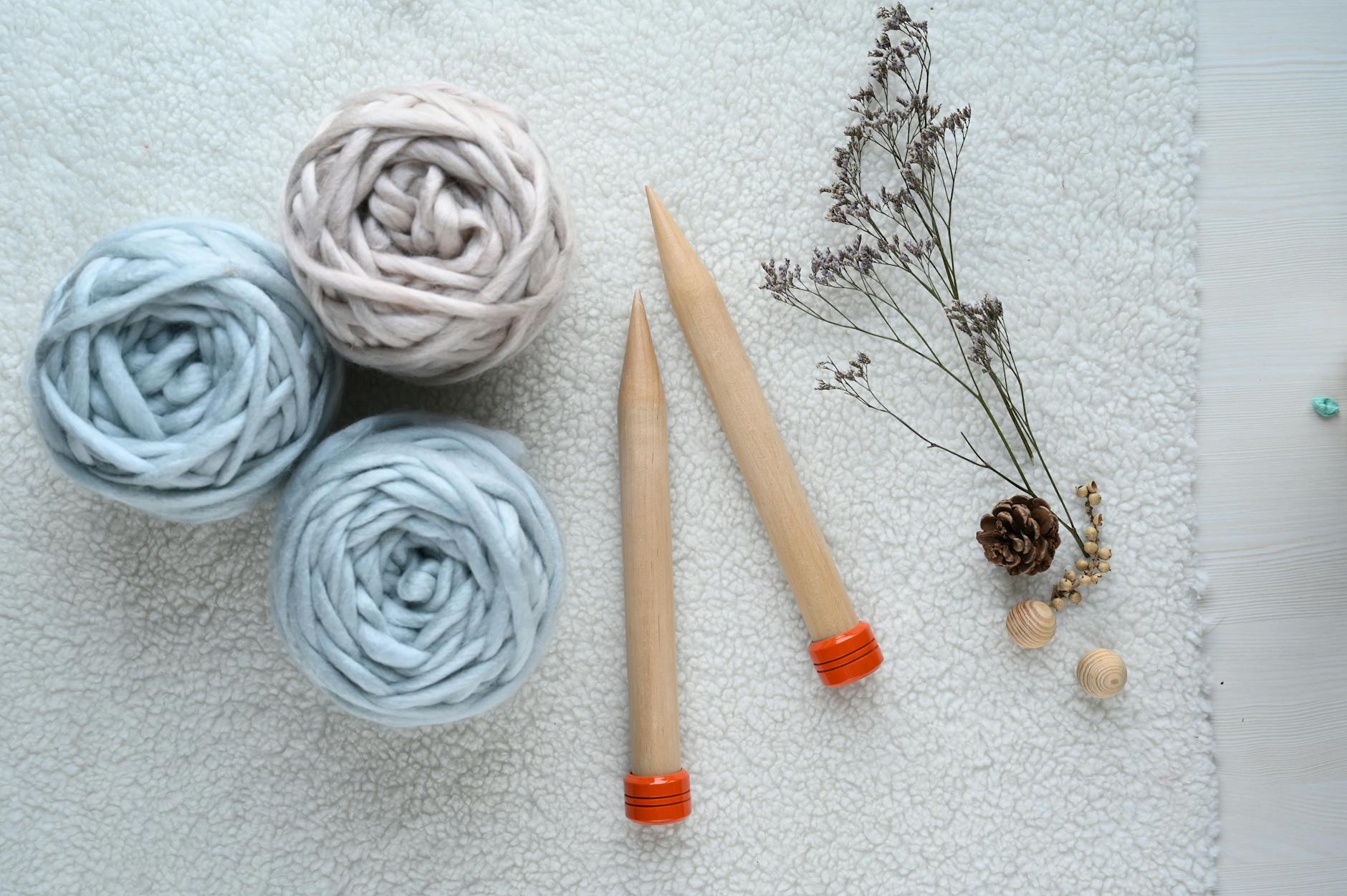 A flat lay of knitting supplies including wool yarn balls and needles on a soft surface.