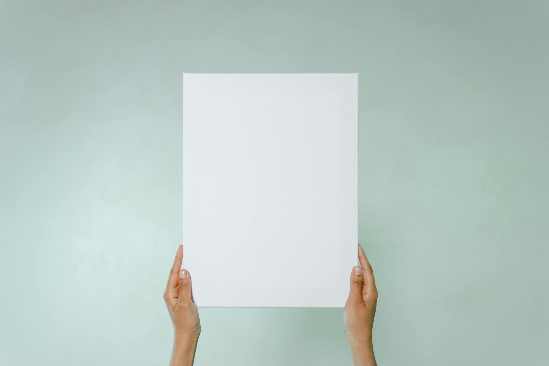 Simple blank canvas held hands on light green background with copy space.