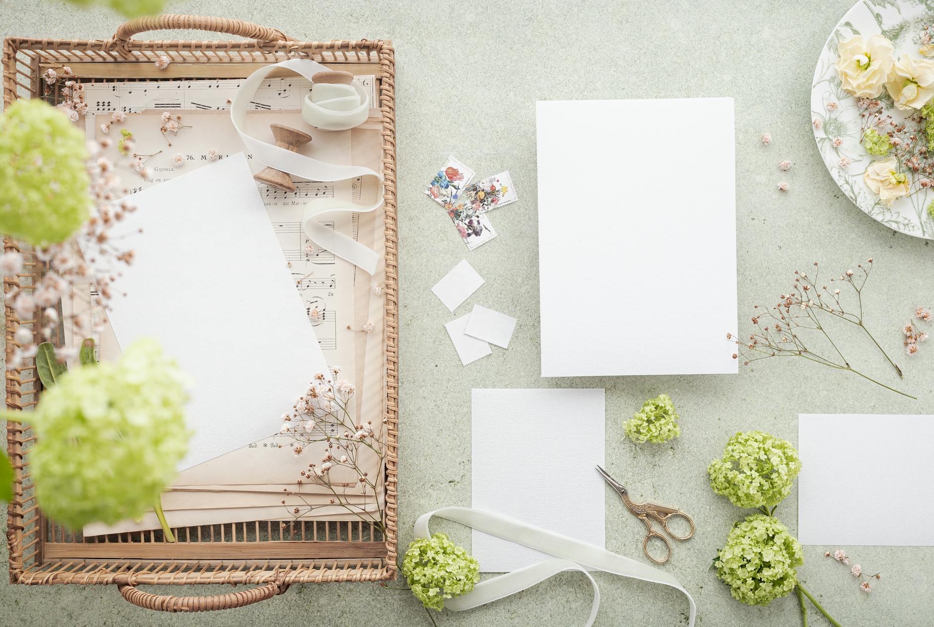 A styled flat lay featuring wedding invitations with green floral accents and stationery items.